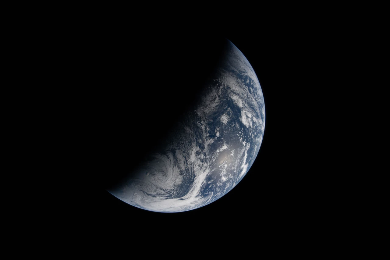 Earth seen from space, with sunlit blue oceans and white clouds on the right and its night side dark on the left.